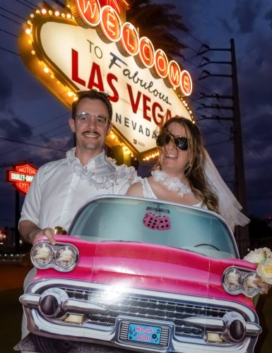 Groom holds a Las Vegas license plate while his bride smiles at the Welcome to Fabulous Las Vegas sign.