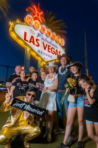 Group of friends and family cheer with an Elvis impersonator at the Welcome to Fabulous Las Vegas sign during a wedding celebration.