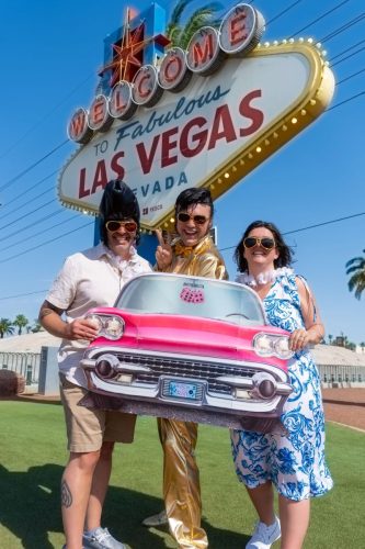 Bride and groom hold a 'Las Vegas' license plate while smiling in front of the Welcome to Fabulous Las Vegas sign with an Elvis impersonator.