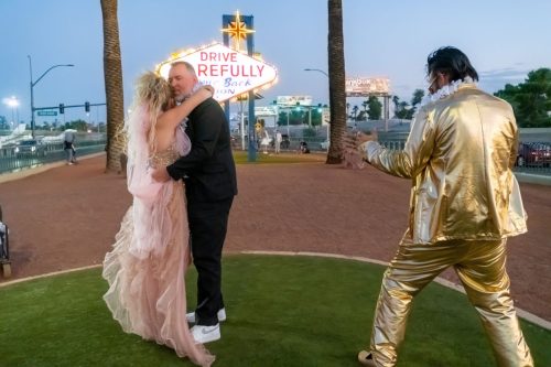 Groom lifts his bride in a romantic dip on a grassy lawn during their Elvis-themed wedding in Las Vegas.