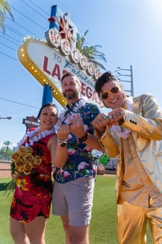 Group of friends cheer with gold-suited Elvis impersonator at the Las Vegas sign during an Elvis wedding.