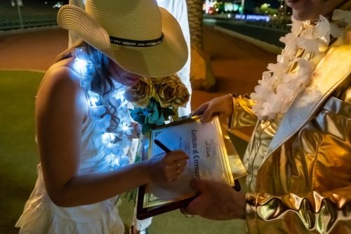 Gold-suited Elvis impersonator rocks out with the bride and groom during their Las Vegas sign wedding celebration.